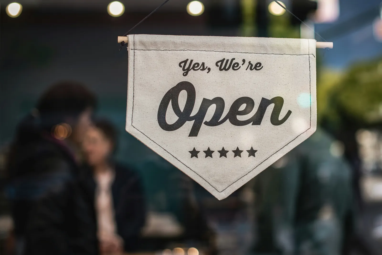 Plaquinha pendurada na vitrine de uma loja com os dizeres "Yes, We're Open"