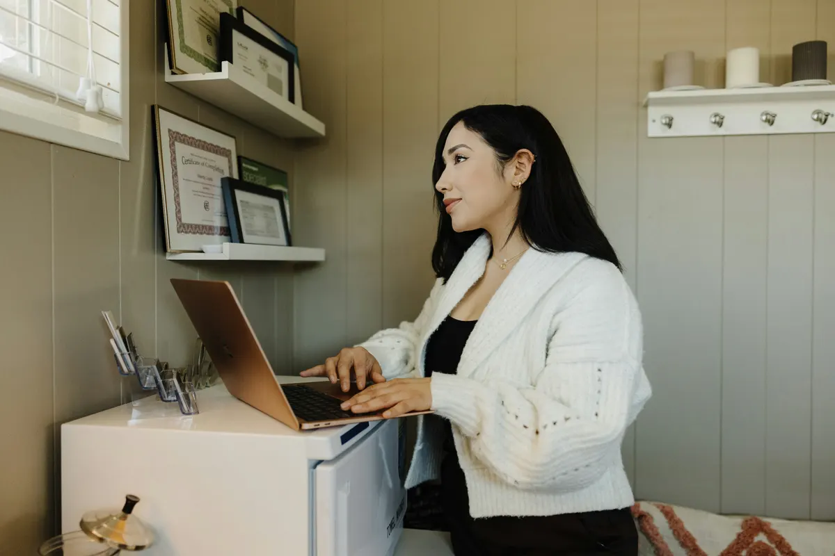 Mulher sentada em uma mesa avaliando opções no notebook antes de decidir sobre o site da empresa